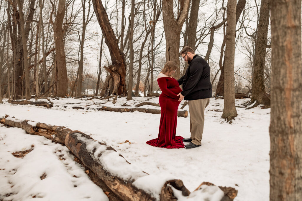 Snowy maternity session at cool creek park, mother is wearing a deep red dress